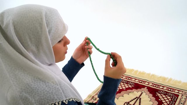 Veiled Muslim Girl with Tasbih Praying on Carpet in Studio