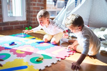 Adorable blonde twins playing with cars around lots of toys at kindergarte