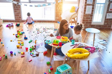 Young beautiful teacher and toddlers playing on the table with lots of toys at kindergarten