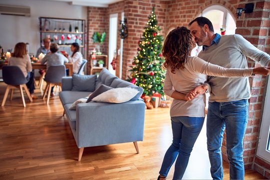 Family and friends dining at home celebrating christmas eve with traditional food and decoration, romantic couple dancing in love