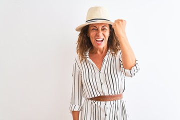 Obraz na płótnie Canvas Middle age businesswoman wearing striped dress and hat over isolated white background angry and mad raising fist frustrated and furious while shouting with anger. Rage and aggressive concept.