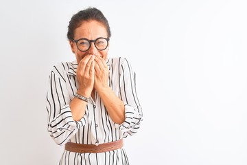 Middle age businesswoman wearing striped dress and glasses over isolated white background laughing and embarrassed giggle covering mouth with hands, gossip and scandal concept