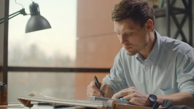 Architect man sits at drafting table in modern industrial office during the day