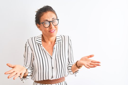 Middle age businesswoman wearing striped dress and glasses over isolated white background clueless and confused with open arms, no idea concept.