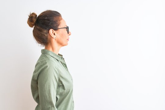 Middle age woman wearing green shirt and glasses standing over isolated white background looking to side, relax profile pose with natural face with confident smile.