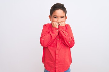 Beautiful kid boy wearing elegant red shirt standing over isolated white background looking stressed and nervous with hands on mouth biting nails. Anxiety problem.