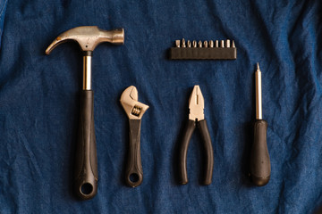Hand tools such as hammers, pliers, wrench and screwdrivers are arranged on a blue denim background.