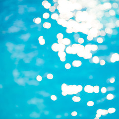 Naklejka na ściany i meble Bokeh light effects over a rippled, blue water background