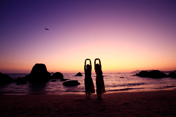 Two women by the sea, silhouetted by the setting sun