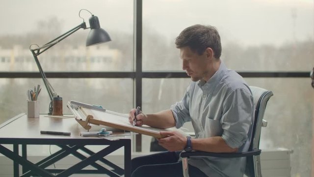 Architect man sits at drafting table in modern industrial office during the day