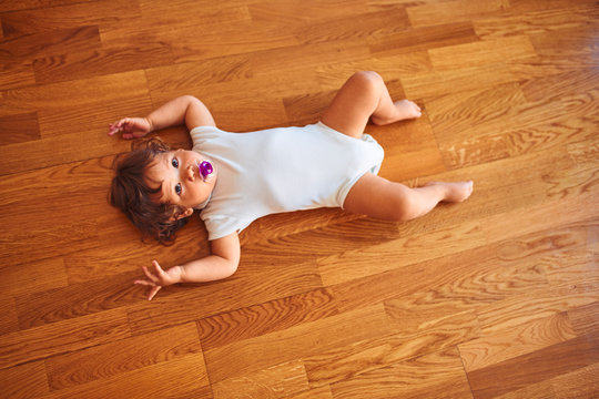 Beautiful toddler child girl wearing white bodysuit lying down on the floor using pacifier