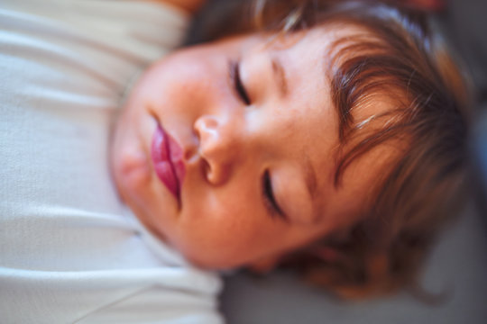 Beautiful toddler child girl wearing white bodysuit lying down on the sofa