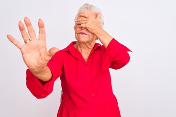 Senior grey-haired woman wearing red casual shirt standing over isolated white background covering eyes with hands and doing stop gesture with sad and fear expression. Embarrassed and negative