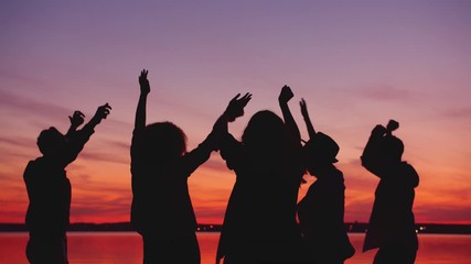 Cheerful students girls and guys are dancing on beach at sunset relaxing at outdoor party together enjoying music and dance. Friendship and nature concept.