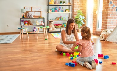 Beautiful teacher and blond toddler girl building tower using plastic blocks at kindergarten