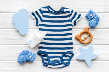 Blue bodysuit for baby boy near children's accessories on white wooden background top-down