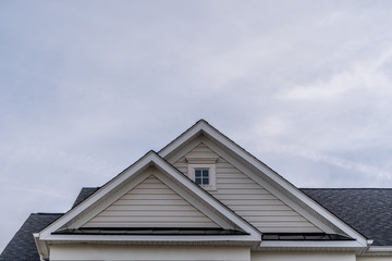 Reverse double gable close up on luxury single family residential home.  Square single pane gable window. Roof line of traditional home with one gable running one way reverse gables running the other.