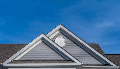 Reverse double gable close up on luxury single family residential home.  White round louver vent. . Roof line of traditional home with one gable running one way reverse gables running the other.