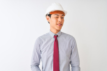 Chinese architect man wearing tie and helmet standing over isolated white background winking looking at the camera with sexy expression, cheerful and happy face.
