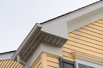 Horizontal vinyl siding, white frame gutter guard system, fascia, drip edge, soffit, on a pitched roof attic at a luxury American single family home neighborhood USA