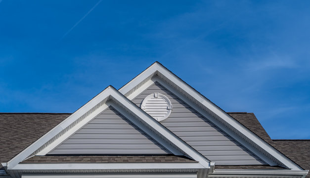 Reverse double gable close up on luxury single family residential home.  White round louver vent. . Roof line of traditional home with one gable running one way reverse gables running the other.