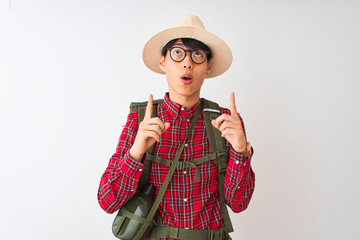 Chinese hiker man wearing backpack canteen glasses hat over isolated white background amazed and surprised looking up and pointing with fingers and raised arms.