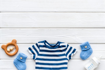 Newborn baby boy set - blue clothes as bodysuit, booties, toys - on white wooden table top-down frame copy space