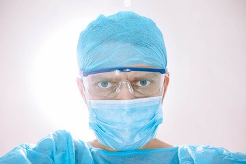 Doctor surgeon in uniform and glasses looks at the camera, the patient back bright light in the operating room.