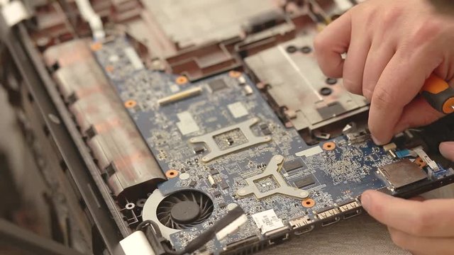 Closeup of technician hands repairing laptop computer cooling system.