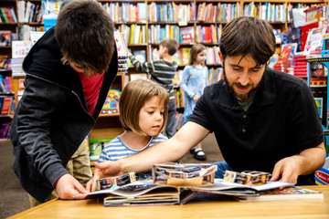 Young girl reading book at bookstore with Dad