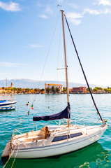 Garda lake western shore, Lombardy, Northern Italy. View on parked white sailing yacht on crystal...