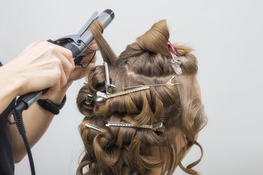 Professional hairdresser twists the hair with a curling iron in beauty salon. Create the image of the bride blonde. Close up.