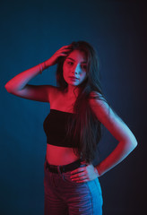Slim, beautiful young girl in black top posing in neon red and blue light