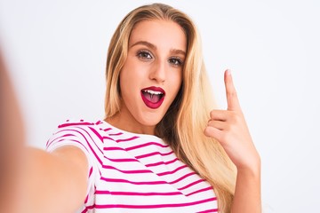 Beautiful woman wearing striped t-shirt make selfie by camera over isolated white background surprised with an idea or question pointing finger with happy face, number one