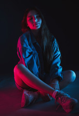 Slim, beautiful young girl in black top posing in neon red and blue light