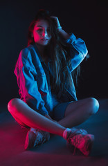 Slim, beautiful young girl in black top posing in neon red and blue light