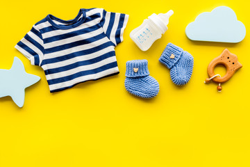Baby background - blue color. Clothes and accessories for newborn boy on yellow table top-down frame copy space