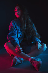 Slim, beautiful young girl in black top posing in neon red and blue light