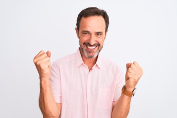 Middle age handsome man wearing casual pink shirt standing over isolated white background celebrating surprised and amazed for success with arms raised and open eyes. Winner concept.