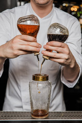 Bartender prepairing a cocktail at the bar, adding bitters into a shaker