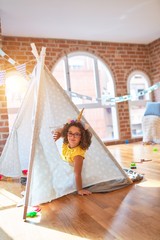 Beautiful toddler wearing glasses and unicorn diadem sitting on the floor inside tipi at...