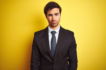 Young handsome businessman wearing suit and tie standing over isolated yellow background skeptic and nervous, frowning upset because of problem. Negative person.