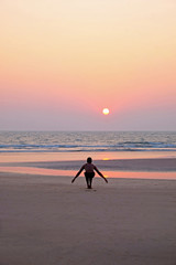 An unrecognizable man doing a yoga the sun salutation on an empty beach at sunset