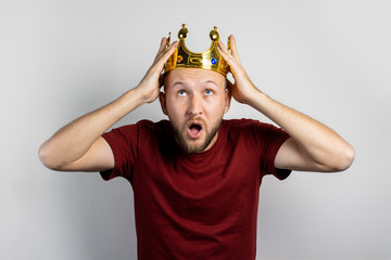 Young man with a crown on his head and a surprised face on a light background. Concept is king, luck, gain, rich, dream, goal, aspiration. Banner