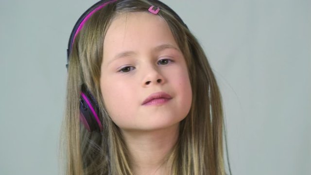 Pretty smiling cild girl listening to music in big pink earphones.