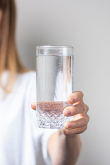 Young woman holds a glass with clear water on a light background. Banner. Concept of thirst, heat, health and beauty care, water balance © Alex
