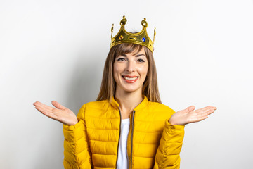 Young woman in a yellow jacket and a gold crown on a light background. Emotion laughter, surprise,...