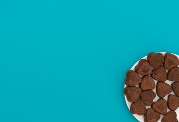 Heart-shaped chocolates in white bowl on blue background. Valentine's Day concept. Valentine greeting card. Flat lay style with copy space.