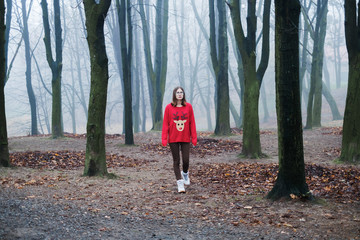 The young girl in the red sweater is walking alone in the cold foggy forest