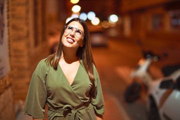 Young beautiful girl smiling happy and confident walking at the town street, standing with a smile on face around night lights bokeh